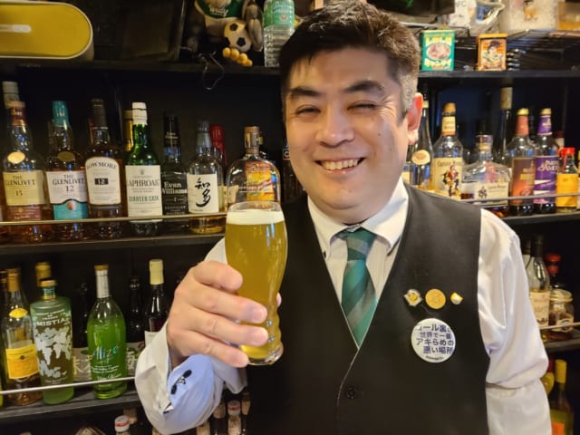 『Restaurant Bar STOLAS』の村岡和寿さん。笑うバーテンダー。緑色をきれいに出すには、しばらく瓶を逆さまにしてから注ぐのがコツとのこと（クラブ関係者談）。